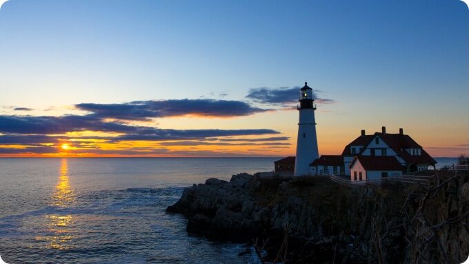 light house on a small cliff face at sunset